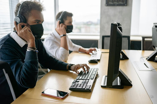 IT support agents wearing headsets and face masks working at desktop computers in a modern office.